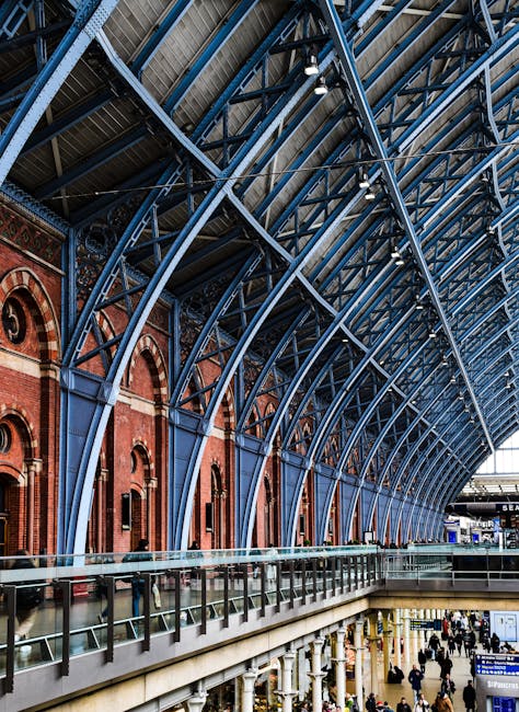 The interior architecture of St Pancras station features a large, curved metallic roof structure supported by blue-painted steel arches, with a combination of red brick walls and arched windows along 